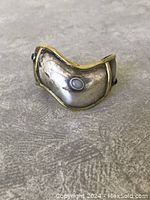 Front angle of curved silver-tone cuff with yellow metal borders and three bezel-set cabochons in black, white, and green.