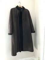 Full view of a long dark brown shearling coat hanging on a hanger, buttons visible, showing front side.