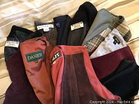 Top view showing inner linings and brand labels of nine folded vintage vests in various styles and colors