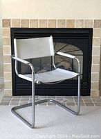Side angle of chair showing tubular chrome frame and worn white leather seat and backrest with armrests.