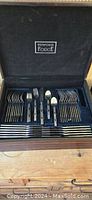 Open box showing the set of Wexford Forge cutlery including forks, knives, spoons, and serving utensils arranged inside velvet-lined compartments.