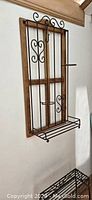 Wood and wrought iron wall-mounted plant stand with curved scroll details and small shelf.