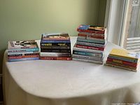Wide shot of all 29 books in different stacks on a white table in front of a window with green wall background.