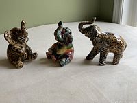 Three elephant figurines with varying patterns and colors, shown front view on white surface near window.