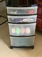 Full view of the 4 drawer plastic storage tower on wheels with contents visible through semi-transparent drawers, including ribbons and trims.