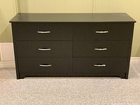 Front view of black dresser with six closed drawers, showing metal handles, smooth finish, modern style.