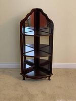 Frontal photo of dark wooden corner display cabinet showing three glass shelves and mirrored back panel.