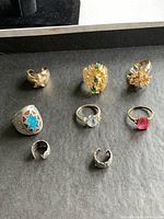 Top-down photo showing nine rings arranged on a flat surface, highlighting various colors, designs and materials including gold and silver tones.