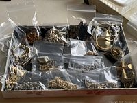 Top view of 15 necklaces individually bagged in a box showing variety of metal finishes and chain styles