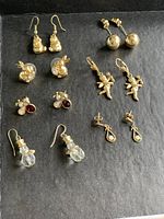 Photo showing a variety of gold tone earrings arranged on a dark background including Winnie the Pooh, bunnies, bugs, cupids, gold balls and opal drop designs.