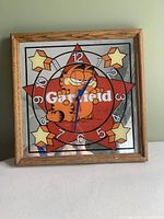 Front view of Garfield wall clock showing character, star design, numbers, and clock hands inside oak frame.
