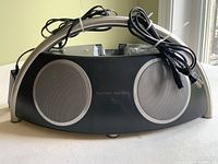 Front view of the Harman Kardon iPod dock speaker with two large circular speaker grilles and an arching handle on top with cords bundled.