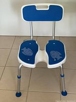 Front view of shower/bath chair showing seat with fish design and metal legs with blue caps