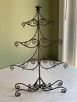 Front view of metal Christmas tree-shaped ornament holder with decorative scrollwork and hooks for ornaments.