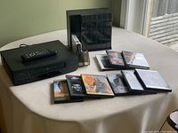 General view of lot items on table including GE VCR, remote, VHS storage system, 1 VHS tape, and 9 DVDs.