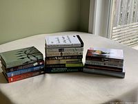 Three stacks of novels on a table, with various titles and authors visible.