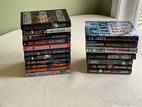 Stack of 18 paperback novels by Iris Johansen and J.A. Jance on light cloth surface.