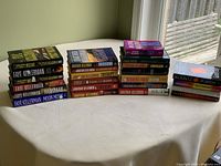 Wide view of 23 novels stacked on table showing variety of authors and titles.