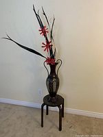Full view of wooden four-leg plant stand with metal vase and faux flowers arranged inside.