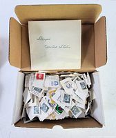 Photo of open cardboard box filled with numerous loose vintage stamps mostly attached to cut pieces of paper, also showing an envelope labeled United States stamps inside the box
