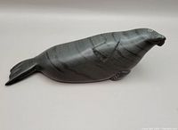 Front and side view of the dark grey Inuit stone carving shaped like a seal, showing natural stone pattern and smooth finish.