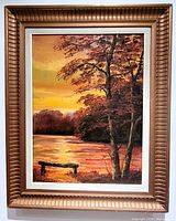 Full view of the framed oil painting showing an autumn lakeside scene with bench and trees, signed by the artist.