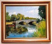 Full view of framed oil painting showing scenic river with bridge, rowboat, trees, and reeds.