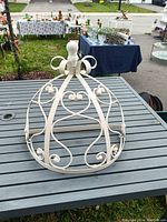White metal dome-shaped bed canopy crown with decorative scrollwork and a finial on top, placed on a outdoor table.