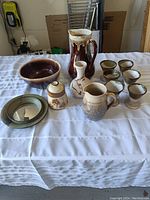 Full view of all pottery items including bowl, pitchers, goblets, and plate laid out on white cloth