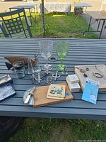 Photo of the lot on outdoor table showing all items, including goblets, wine stoppers, keychains, cheese board, and coasters.