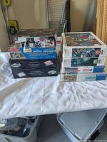 Photo showing stacks of assorted boxed puzzles and games with various piece counts including a Buffalo Pets puzzle and Light Up Checkers set.