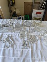 Overall collection of clear glass animal figurines displayed on white cloth, including lion, dog, bird, ram, and others.