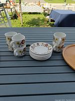 Full view of cups stacked and saucers arranged in front, placed on an outdoor table with some trays visible to the right.