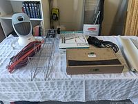 Overview of lot items on table showing heater, shower caddies, tap set in box, extension cords and some manuals.