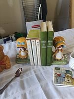 Photo showing vintage Holly Hobby bookends holding multiple Louisa May Alcott books on a tablecloth with other items visible around.