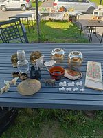 Overview of Mid Century Modern decor lot on outdoor table showing glassware, stone figurines, brass dish, bookends, and note pad
