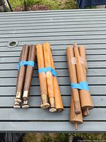 Three sets of mid-century modern style furniture legs on a gray slatted table outdoors. Each set bundled with blue and tan tape.