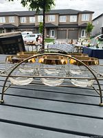 Photo showing six clear roly poly glasses with thick gold rims seated in a gold metal holder with rounded arches and handle.