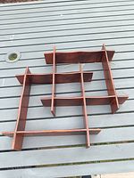 Photo of wooden mid-century modern wall shelf lying flat on a gray outdoor table showing the grid structure and finish.