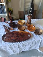 Overview of all wooden items on a white cloth: tray, bowls, utensils, pepper grinder, candle holder.
