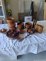 Photo showing large wooden pillar candle holder, several wooden bowls (including stacked sets), Oregon myrtlewood napkin holder, two wooden grinders (salt and pepper), small wooden apple shaped dish, wooden utensils and more, arranged on a table.