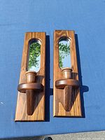 Two rectangular wooden Mid-Century Modern style wall sconces with mirrors and candle holders photographed side by side on a blue surface.