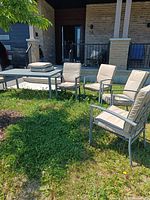 Patio set including grey metal table and four cushioned chairs in outdoor setting.