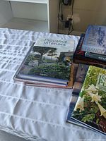 Six hardcover books placed on a white striped fabric. Titles visible include Provence Interiors, France, and The Complete Guide to Indoor Plants.