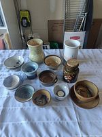Wide view of 11 ceramic pottery items on a white cloth, showing a mix of bowls, vase, and jar with cork stopper