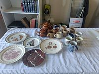 Photo of teapot, multiple mugs, creamers, and assorted decorated plates on table