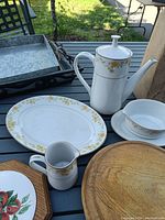 Porcelain Noritake Chorus china pieces including coffee pot, cream pitcher, cup and saucer, and oval platter placed on table along with other trays and wooden bowl holder.