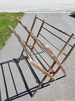Full view of the vintage wooden folding blanket rack outdoors on pavement showing the rack's folding design and wooden rods.