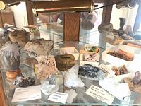 Wide view of various mineral specimens on a glass shelf with display lighting including iron pyrite labeled from La Rioja, Spain.