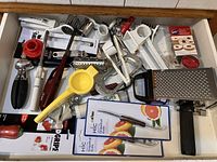 Image showing a drawer packed with assorted kitchen utensils including several graters, citrus juicer, grapefruit tools, strawberry huller, rolling cheese grater, and miscellaneous kitchen gadgets.